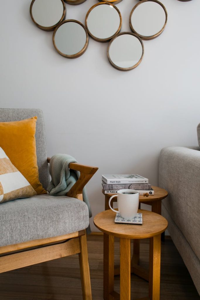 A modern and cozy living room corner featuring an armchair with cushions, decorative mirrors, and a coffee table with books.